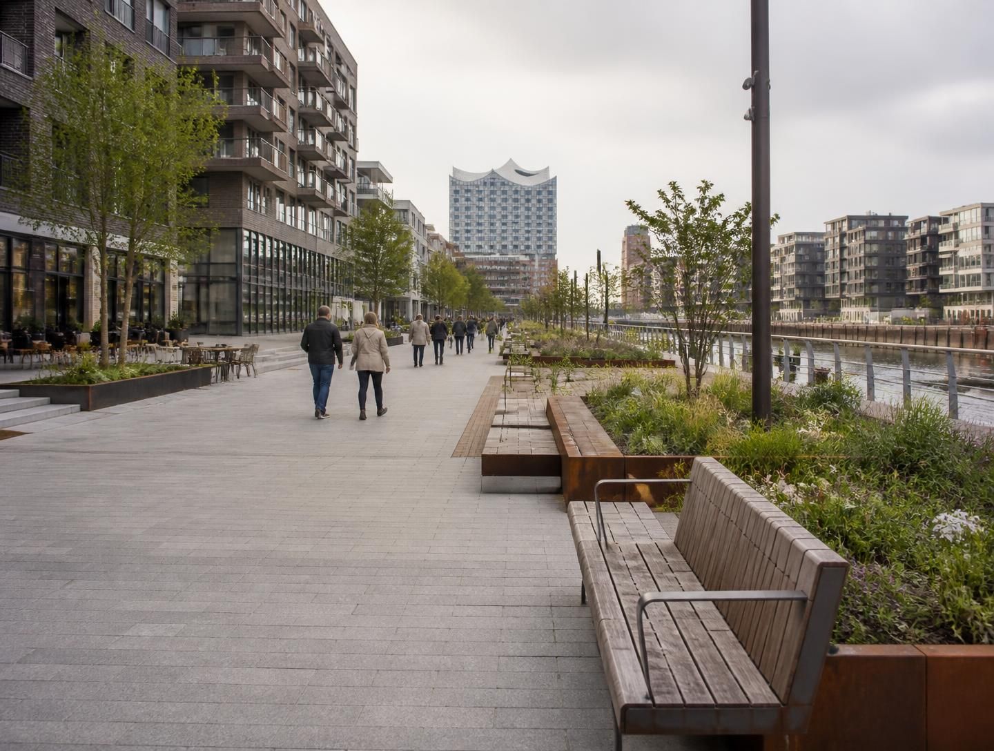 Paseo público con pérgola metálica verde y pavimento de piedra