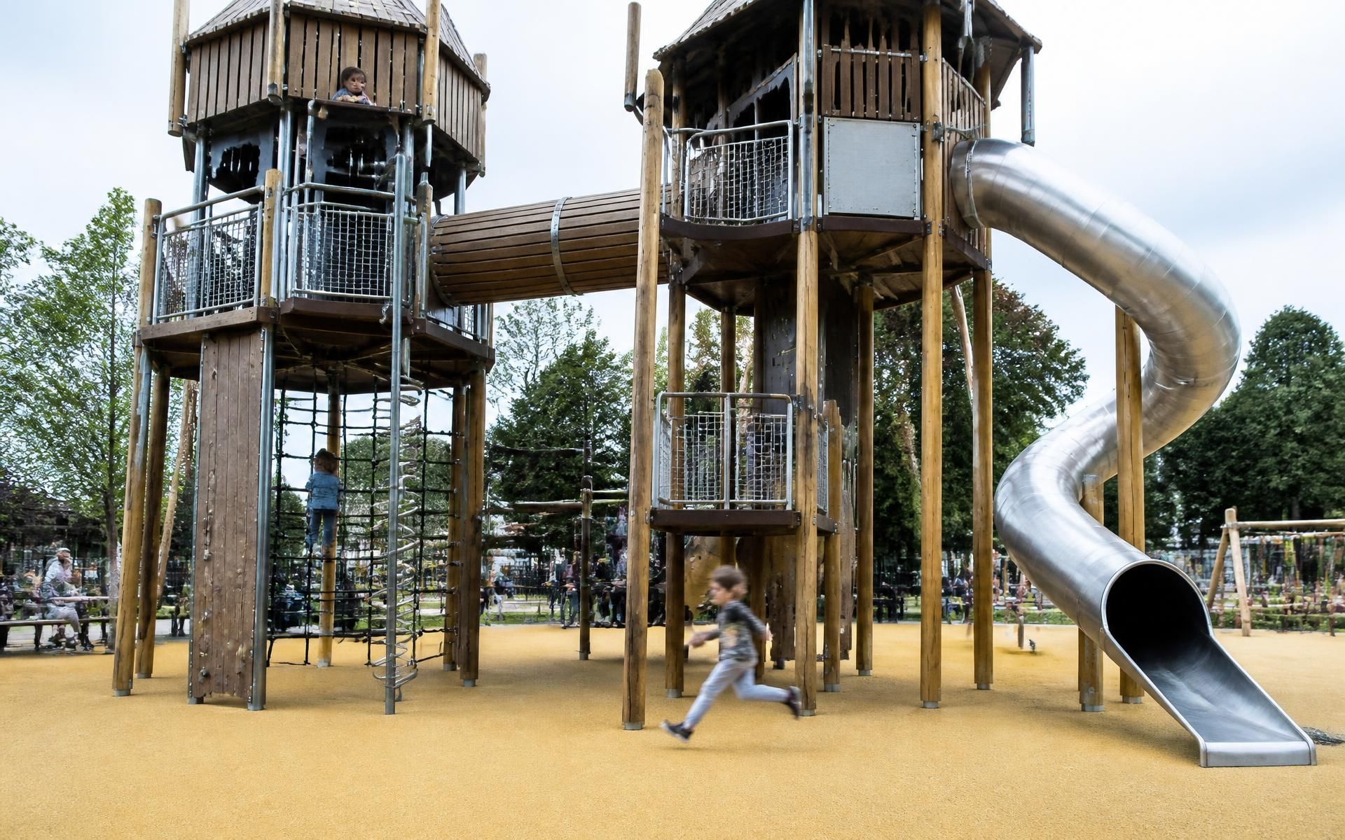 Estructura multijuego de acero verde y madera con rampas, redes y tobogán en un parque